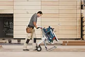 A person wearing safety equipment moves a saw stand across a wood workshop floor.