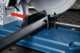 Metal cut-off saw cutting a square metal pipe on a blue work surface.