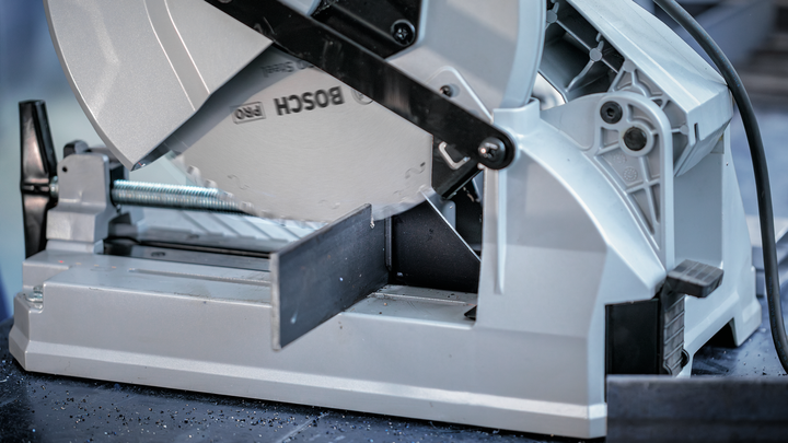 Metal cutting saw blade slices through a steel bar in a workshop setting.