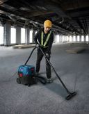 A person wearing safety equipment uses a wet dry extractor to clean a construction site floor.
