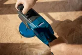 A person operates a blue cordless angle drill on a wooden surface.