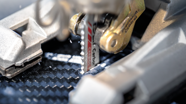 Jigsaw blade cutting through a carbon fiber sheet.