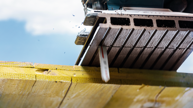 Saw blade cuts through a wooden beam in bright outdoor light.