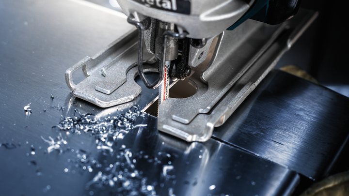 Jigsaw cutting a sheet of metal, small metal shavings scattered around the blade.