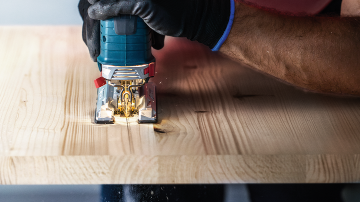 Person wearing safety equipment uses a jigsaw to cut a wooden board.