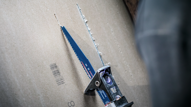 A person cuts drywall using a reciprocating saw blade.