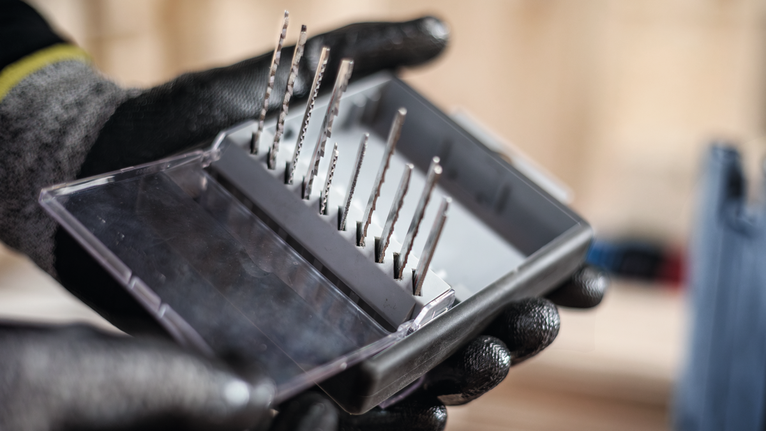 Person wearing safety equipment holds a set of jigsaw blades in a case.