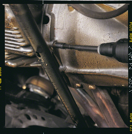 Avvitatore a trapano che stringe una vite su un carter metallico del motore.