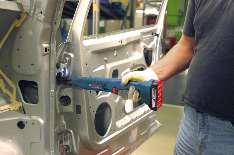 Una persona che indossa un dispositivo di sicurezza utilizza un utensile senza fili per fissare una cerniera all'interno della portiera di un'auto.