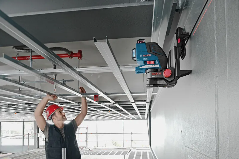 Una persona che indossa un'attrezzatura di sicurezza allinea i telai del soffitto utilizzando uno strumento di livellamento laser su un supporto universale.