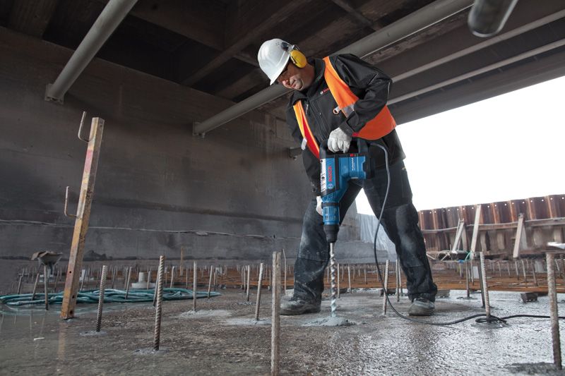Una persona che indossa dispositivi di sicurezza perfora il cemento con un martello perforatore in un cantiere edile.