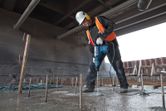 Una persona che indossa dispositivi di sicurezza perfora il cemento con un martello perforatore in un cantiere edile.