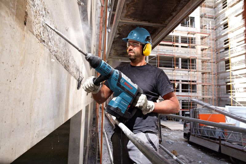 Una persona che indossa dispositivi di sicurezza fora un muro di cemento in un cantiere edile.