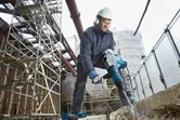 Una persona che indossa un equipaggiamento di sicurezza utilizza un martello perforatore per rompere il cemento in un cantiere edile.