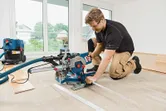 Una persona che indossa dispositivi di sicurezza aziona una sega troncatrice scorrevole per tagliare i pavimenti in ambienti interni.
