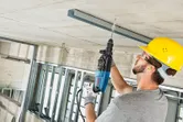 Una persona che indossa un equipaggiamento di sicurezza perfora un soffitto di cemento con un martello perforatore.