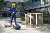 Una persona che indossa un equipaggiamento di sicurezza utilizza un'idropulitrice ad alta pressione per pulire un'unità esterna.