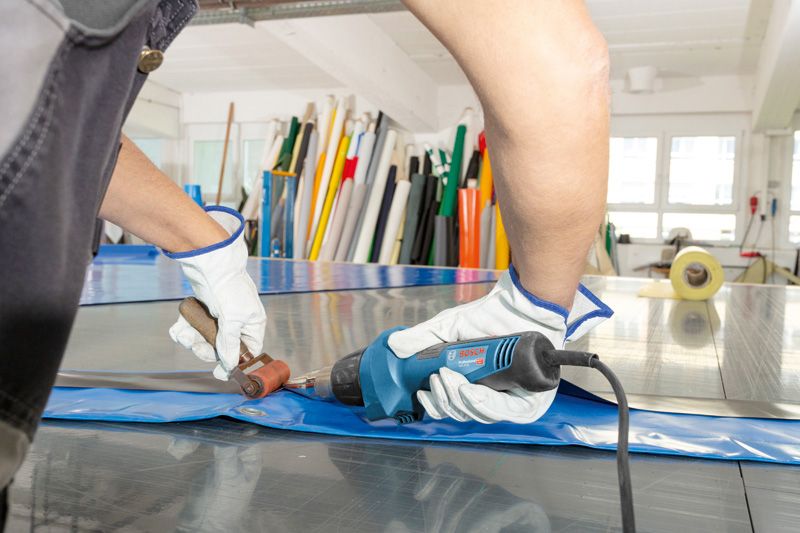 Una persona che indossa un equipaggiamento di sicurezza salda un telo di plastica utilizzando una pistola termica.