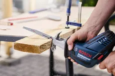 Una persona utilizza una sega alternativa per tagliare una tavola di legno su un banco da lavoro.