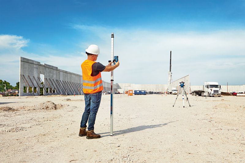 Una persona che indossa dispositivi di sicurezza utilizza uno strumento di livellamento laser in un cantiere edile.