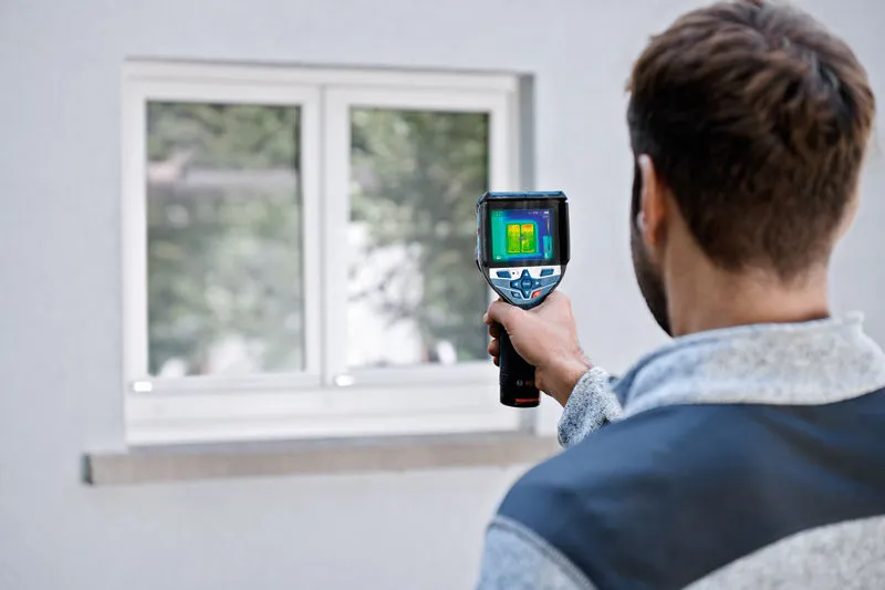 Persona che utilizza una termocamera per ispezionare una finestra.