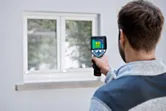 Persona che utilizza una termocamera per ispezionare una finestra.