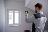 Una persona utilizza una termocamera per ispezionare una finestra in un ambiente interno.