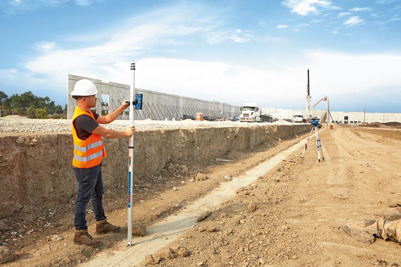 Una persona che indossa un equipaggiamento di sicurezza utilizza un ricevitore laser per misurare il livello del terreno in un cantiere edile.