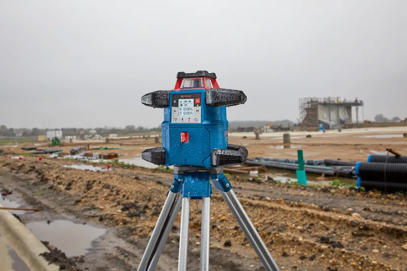 Strumento di livellamento laser su treppiede in un cantiere edile bagnato.
