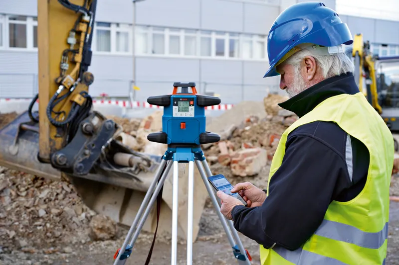 In un cantiere edile, una persona con indosso dispositivi di protezione individuale utilizza una livella laser.