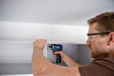 Una persona che indossa un equipaggiamento di sicurezza utilizza un cacciavite a batteria per assemblare un mobile.