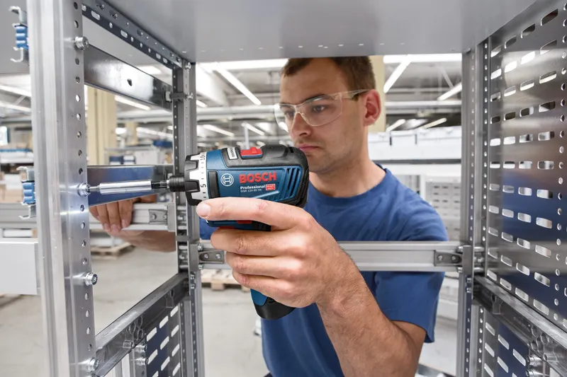 Una persona che indossa un equipaggiamento di sicurezza utilizza un cacciavite a batteria su una struttura metallica.