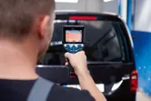 Una persona utilizza una termocamera per scansionare il lunotto posteriore di un furgone nero.