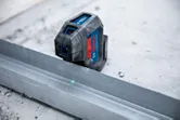 Livella laser che proietta una linea verde su una guida metallica su un pavimento di cemento.
