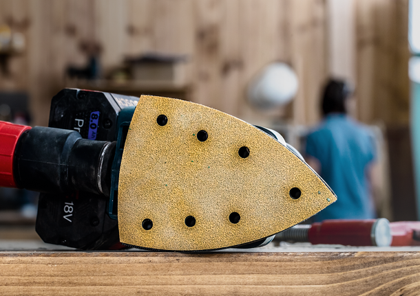 Levigatrice per dettagli appoggiata su una superficie di legno in un'officina, con una persona sullo sfondo.