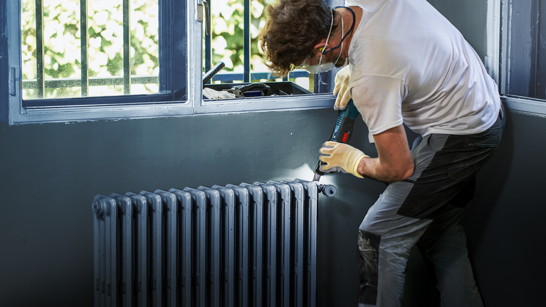 Una persona che indossa l'equipaggiamento di sicurezza si esercita vicino a un termosifone sotto una finestra.