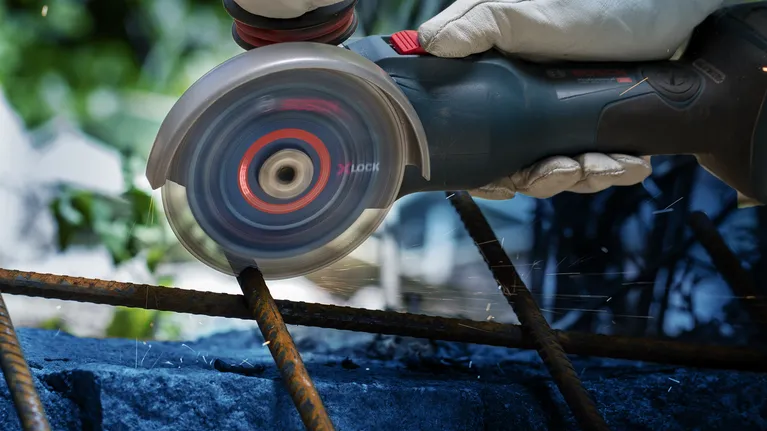 Una persona che indossa dispositivi di sicurezza utilizza una smerigliatrice angolare per tagliare le barre di armatura arrugginite.