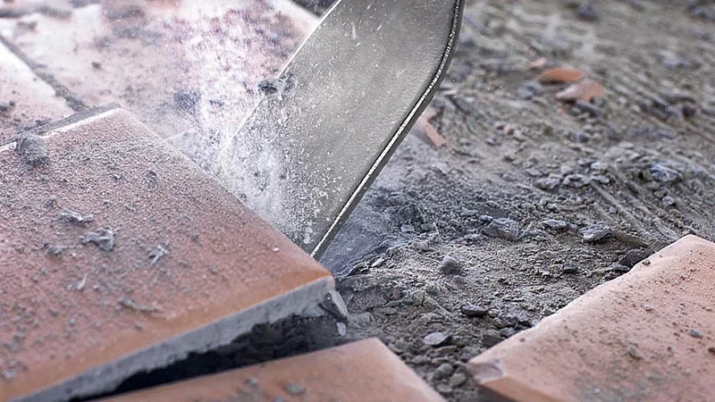 Scalpello per piastrelle che rompe piastrelle di ceramica su un pavimento polveroso.