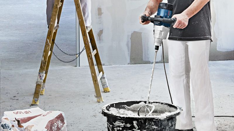 Una persona che indossa un equipaggiamento di sicurezza mescola il materiale in un secchio utilizzando un meccanismo di agitazione.