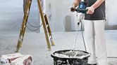 Una persona che indossa un equipaggiamento di sicurezza mescola il materiale in un secchio utilizzando un meccanismo di agitazione.