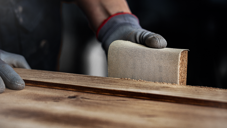 Una persona che indossa un equipaggiamento di sicurezza carteggia una tavola di legno.