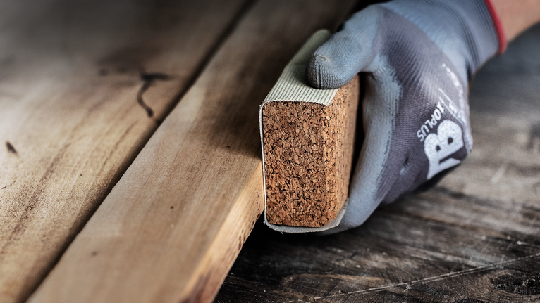 Persona che indossa dispositivi di sicurezza mentre leviga il legno con un blocco abrasivo.