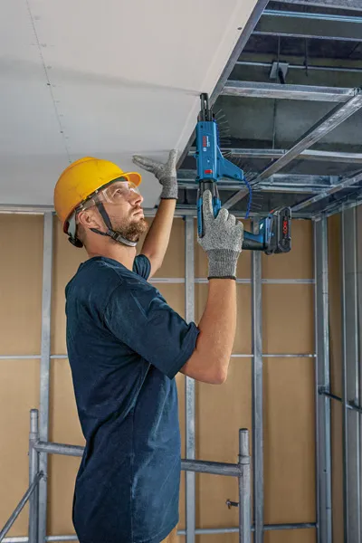 Una persona che indossa un equipaggiamento di sicurezza fissa la struttura metallica del controsoffitto con un utensile elettrico.