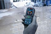 Una persona che indossa dispositivi di sicurezza tiene in mano un misuratore laser in un cantiere edile.