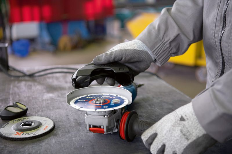 Una persona che indossa un equipaggiamento di sicurezza fissa un disco abrasivo a una smerigliatrice angolare su un banco da lavoro.