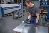 Una persona che indossa un equipaggiamento di sicurezza utilizza una cesoia a batteria per tagliare la lamiera.