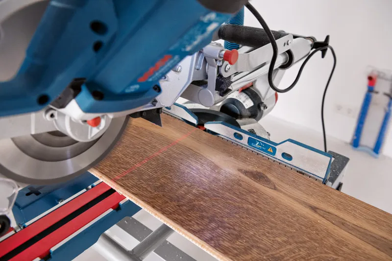 Sega troncatrice con livella laser che taglia un'asse di legno su un banco da lavoro.