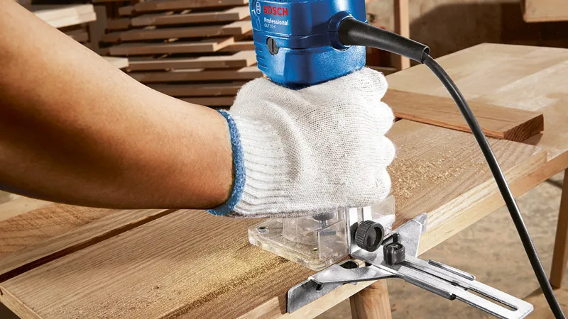 Una persona che indossa dispositivi di sicurezza aziona una fresatrice per legno su una tavola di legno.