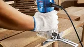 Una persona che indossa dispositivi di sicurezza aziona una fresatrice per legno su una tavola di legno.