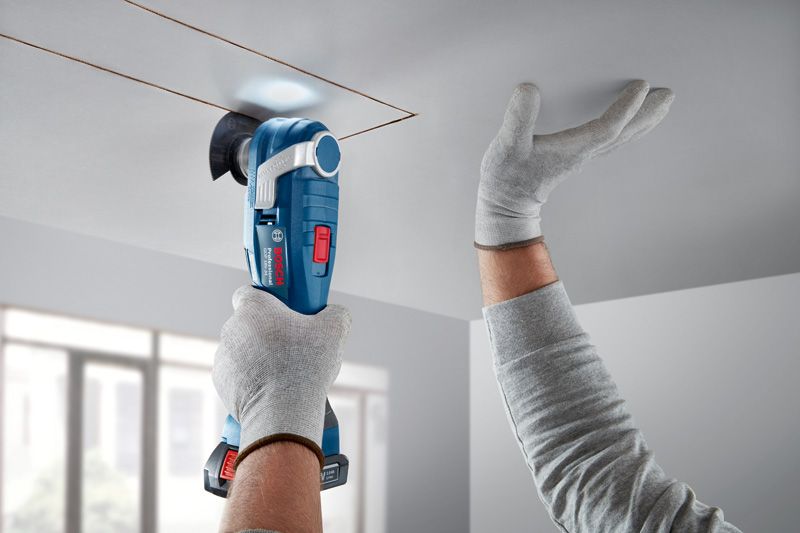 Una persona che indossa un equipaggiamento di sicurezza taglia un pannello del soffitto con un utensile multiuso senza fili.